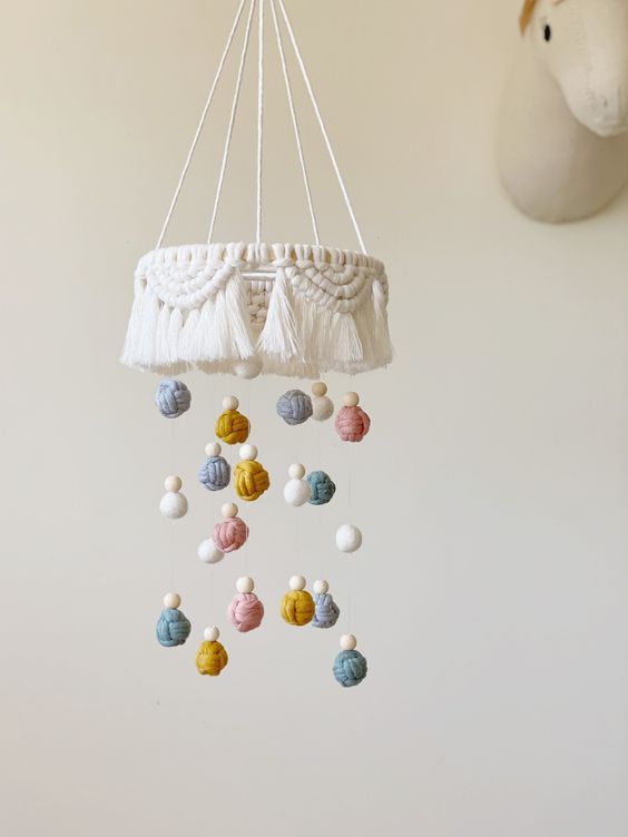 a boho yarn baby mobile with a macrame piece, colorful yarn balls and beads is a stylish idea for a boho space