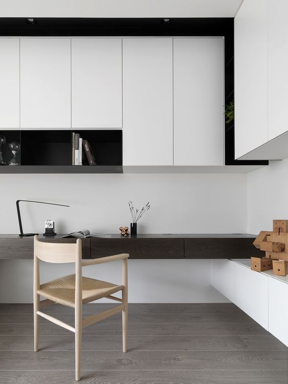 a bold minimalist home office in black and white, with sleek storage units and an open shelf, a built-in dark-stained desk and a woven chair