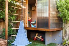 a bold modern playhouse with frosted glass walls to get light in, a sliding door, colorful furniture and a swing attached to the roof