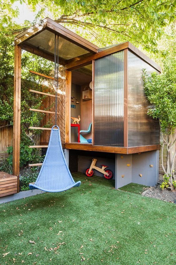a bold modern playhouse with frosted glass walls to get light in, a sliding door, colorful furniture and a swing attached to the roof