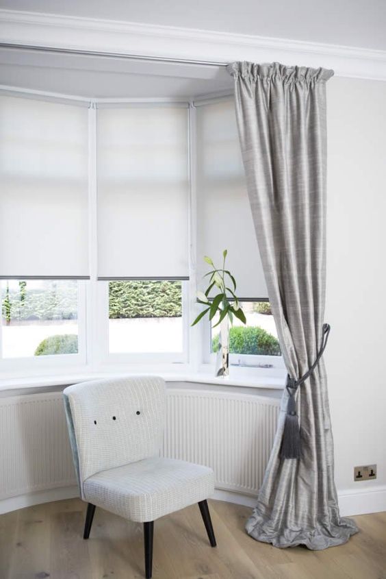 a bow window styled with modern neutral Roman shades looks much cozier and makes this space welcoming