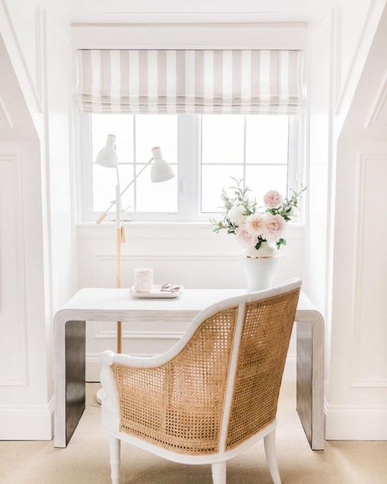 a chic and refined home office nook with a striped Roman shade for more elegance, a stylish modern desk and a rattan chair