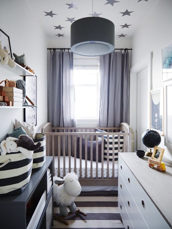 a chic tiny nursery with a stained crib, a white dresser and a black one, a striped rug and printed bedding, a wall-mounted shelf and toys