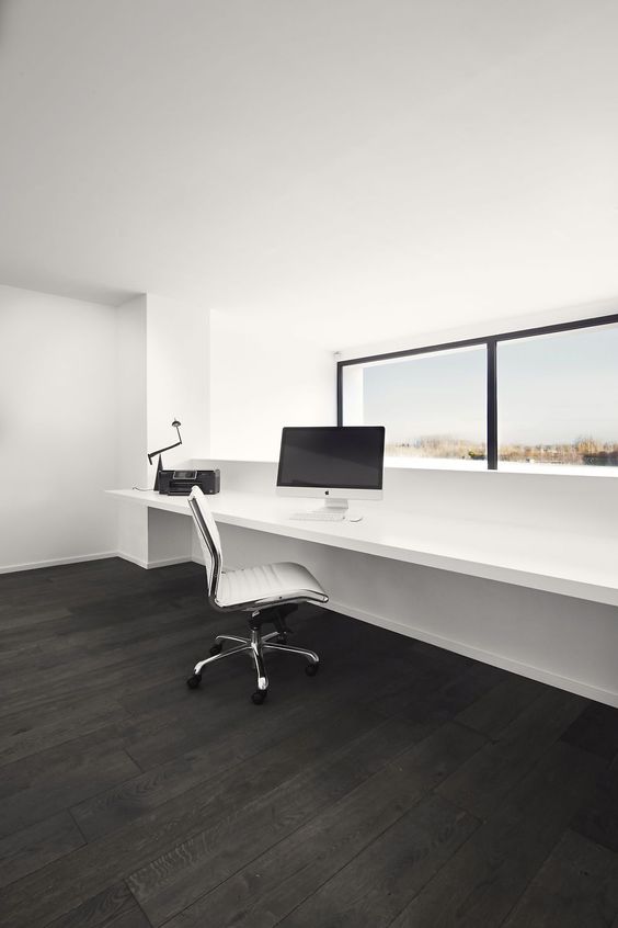 a clean minimalist home office in white, with a dark floor, a window with a view, a floating windowsill desk and a cool white chair