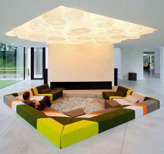 a colorful contemporary conversation pit with a geometric lit up ceiling over it and a fireplace is a unique touch