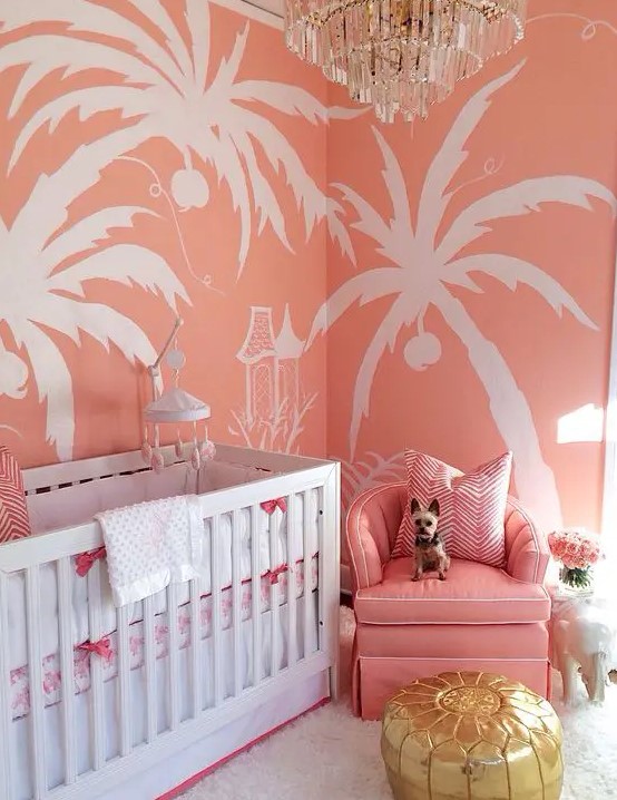 a colorful glam nursery with pink tropical print walls, a pink chair, a glam chandelier and a shiny ottoman