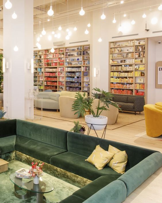 a cool 70s inspired conversation pit with a dark green sofa with pillows, a glass coffee table and pendant bulbs over it