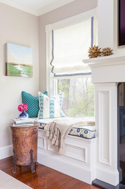 a cool and chic window nook with a Roman shade, a windowsill daybed with printed bedding and a small side table and blooms