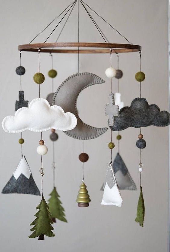a cool woodland nursery mobile with mountains, pompoms, trees, clouds, crosses and a half moon is a stylish forest inspired idea