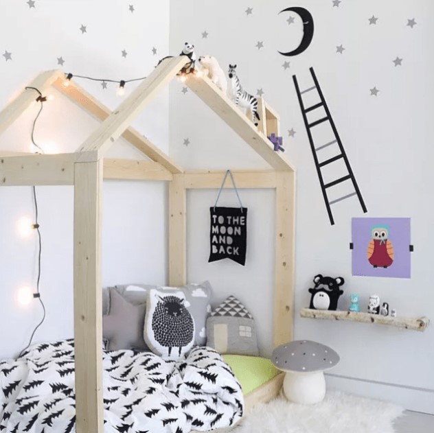a cozy and fun Scandinavian kids' room with a wooden house shaped bed, a shelf, some bright artworks and toys and stars on the walls