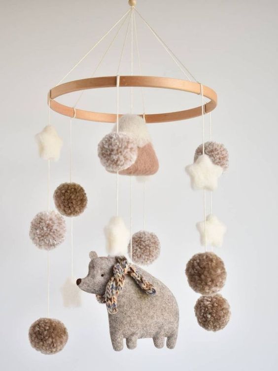 a cozy neutral and pastel mobile of felt and yarn, with a bear in a scarf, pompoms, stars and a mountain is a lovely idea for a mountain themed space