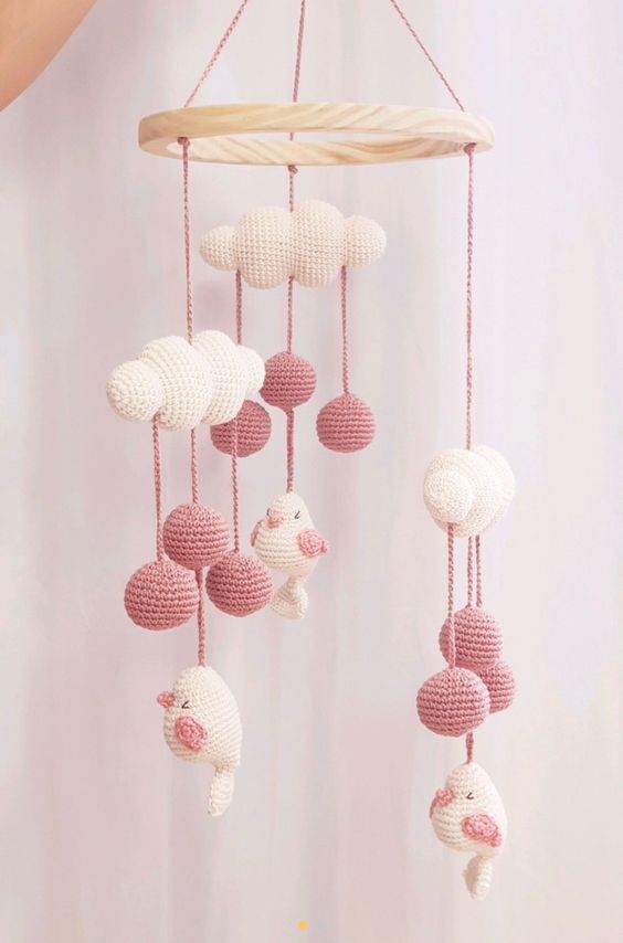 a cute pink and white crochet mobile with clouds, pompoms and birds is a lvoely idea for any kids' space