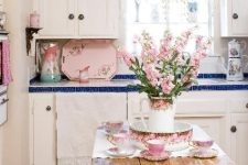 a cute shabby chic kitchen with white cabinets, blue tile countertops, a shabby table and touches of pastel pink