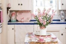 a cute shabby chic kitchen with white cabinets, blue tile countertops, a shabby table and touches of pastel pink