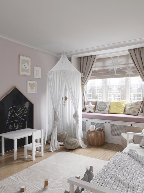 a delicate and subtle Scandi nursery with blush walls, a large windowsill bench with pillows, a bed with neutral bedding and a teepee