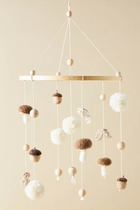 a fall themed nursery mobile with pompoms, wooden beads, mushrooms and acorns is a cool and chic idea