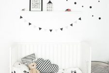 a laconic black and white Scandinavian kid’s room with a white bed, a striped fabric basket, some pillows and a ledge with art