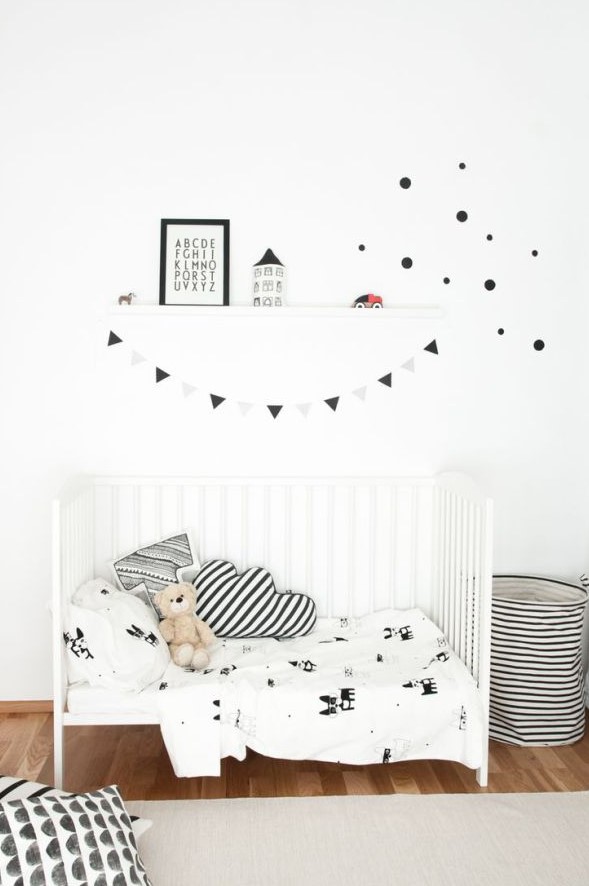 a laconic black and white Scandinavian kid's room with a white bed, a striped fabric basket, some pillows and a ledge with art