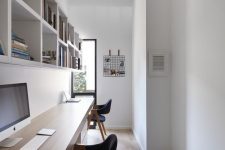 a long and narrow minimalist home office with shelving units and a floating double desk, comfy black chairs and much natural light