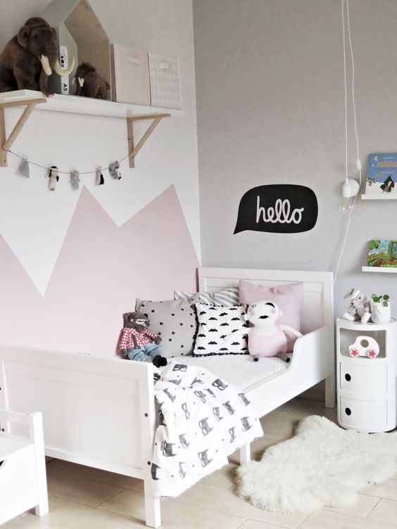 a lovely Scandinavian kid's room with a pink and white accent wall, a white bed with printed bedding, a white shelf and a white nightstand
