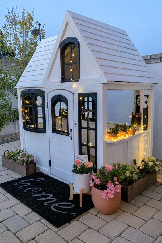 a lovely black and white kids' playhouse with lights, potted plants and blooms, a black rug is a magical space to be