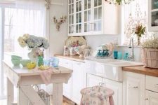a lovely shabby chic kitchen with white cabinets, pastel pink touches, floral prints, a kitchen island and French doors