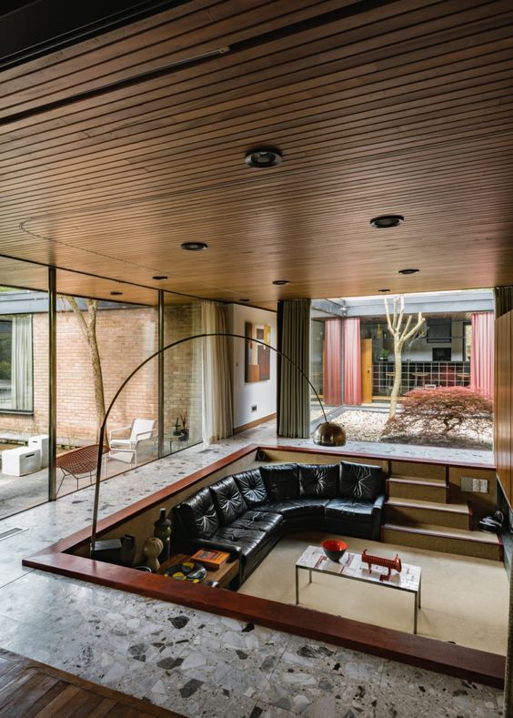 a mid-century modern conversation pit with a black leather sofa, coffee tables, a floor lamp and lovely views through glazed walls