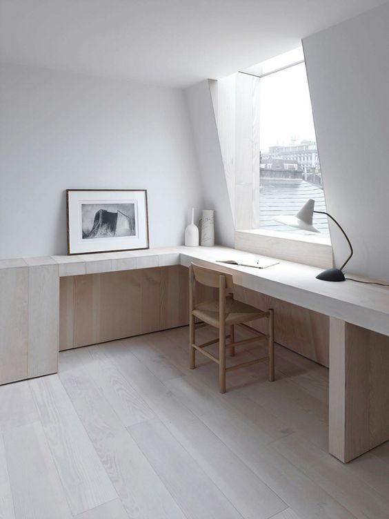 a minimalist and very neutral home office with a view, a built in desk and a chair, a table lamp and an artwork