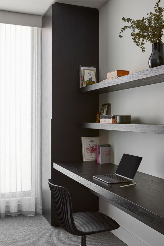 a minimalist home office with a sleek storage unit, open shelves, a built-in desk and a black chair plus greenery in a vase