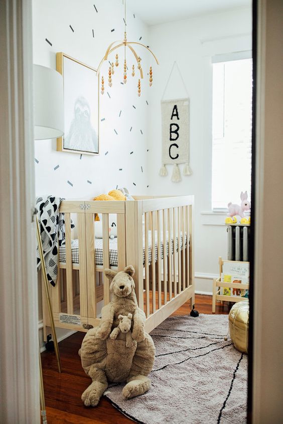 a modern tiny nursery with a stained crib with printed bedding, a changing table, a shelf and some mobiles and toys