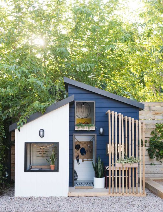 a navy playhouse with a planked porch and a wall-mounted seat, potted greenery looks like a real mid-century modern house