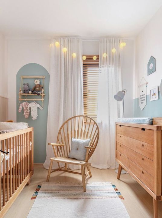 a neutral and pastel nnursery with stained furniture, an accent wall, a makeshift closet and lights and lamps is very welcoming