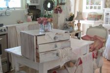 a neutral and pastel shabby chic kitchen and dining space with curtains on the cabinet, lots of floral prints, refined furniture and hanging lamps