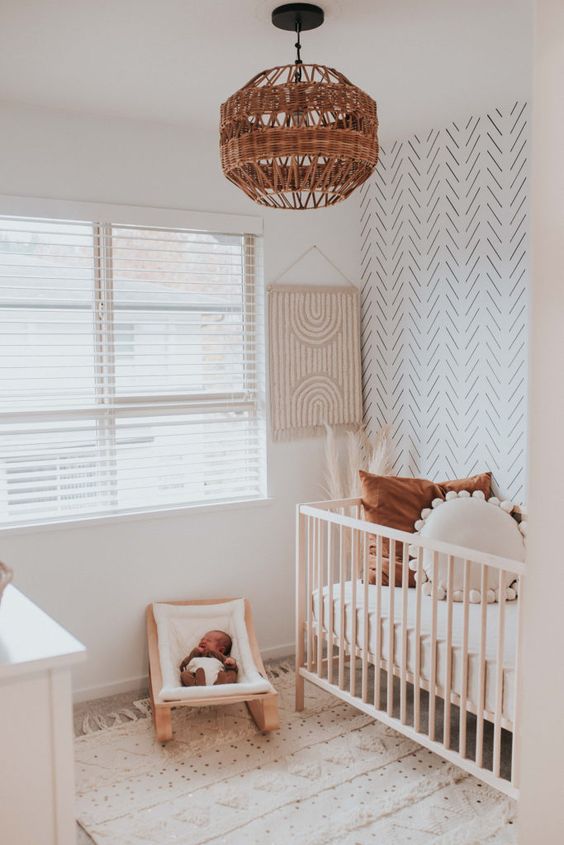 a neutral boho nursery with a white dresser, a stained crib, a tiny rocker for the baby, an accent wall and a printed rug