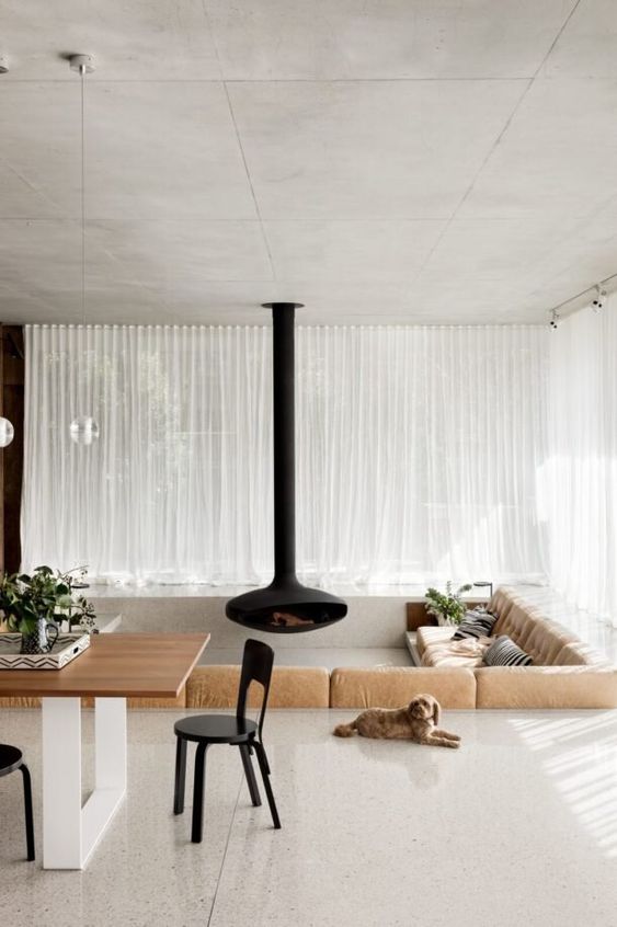 a neutral contemporary conversation pit with a tan sofa along two its sides, a black suspended fireplace and neutral pillows is wow