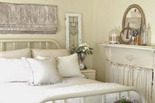 a neutral shabby chic bedroom with buttermilk walls, a metal bed, wooden furniture and a non-working fireplace and a crystal chandelier