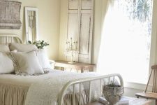 a neutral shabby chic bedroom with buttermilk walls, a white forged bed, wooden furniture, a crystal chandelier and ruffle bedding