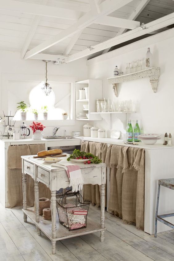 a neutral shabby chic kitchen with cabinets with burlap hanging, a shabby kitchen island, refined shelves and potted greenery