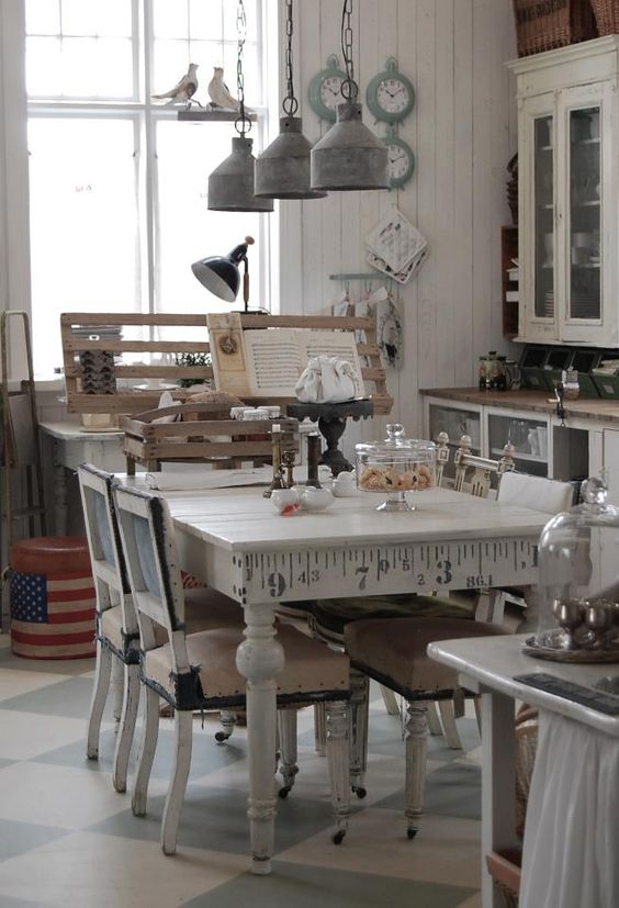 a neutral shabby chic kitchen with white cabinets and glass ones, a vintage table and chairs, metal retro lamps and aqua-colored clocks