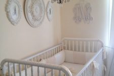 a neutral shabby chic nursery with pastel walls, white vintage furniture, a gallery wall of decorative plates and a small chandelier over the bed