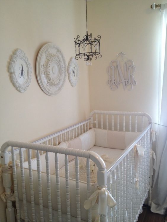 a neutral shabby chic nursery with pastel walls, white vintage furniture, a gallery wall of decorative plates and a small chandelier over the bed