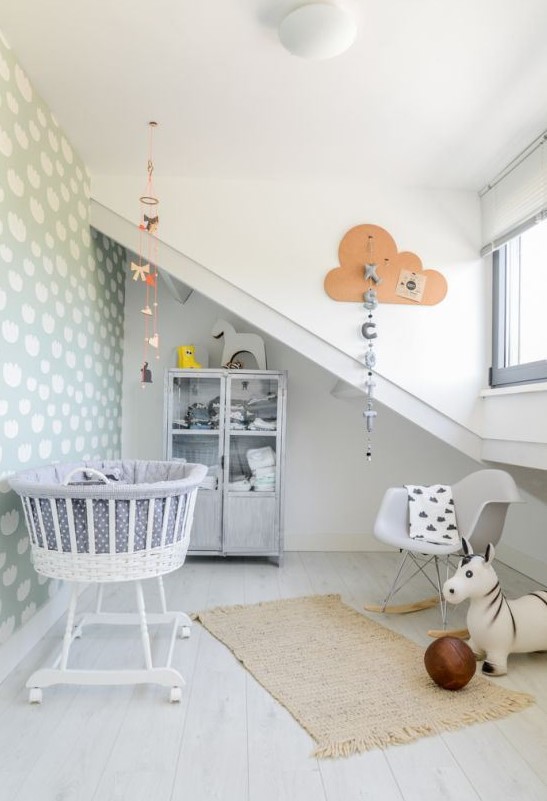 a neutral whimsy nursery with grey walls, a cloud accent wall, printed textiles, mobiles and garlands