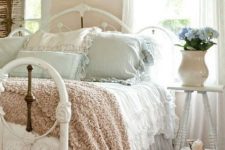 a pastel shabby chic bedroom with peachy walls, a white metal bed, pastel bedding, blooms and vintage shutters