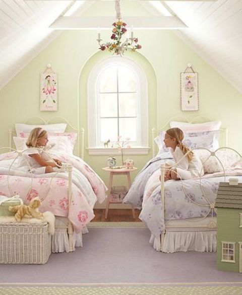 a pastel vintage shared bedroom with a green accent wall, white metal beds, a basket, a floral chandelier and floral bedding