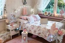 a pink and white shabby chic bedroom with a forged bed, white furniture, pink and floral bedding, candle lanterns and a crystal chandelier
