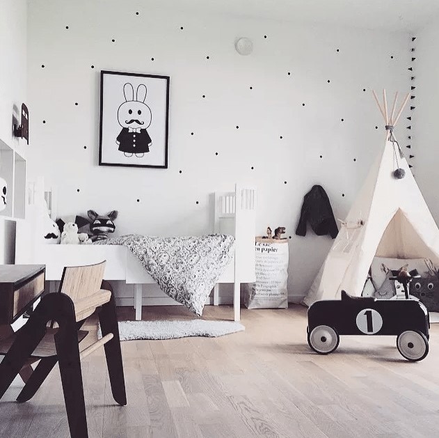 a playful Scandinavian kids' room in black and white, with contemporary furniture, a teepee, a polka dot wall and cool black and white toys