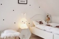 a pretty and airy Nordic kid’s room with a polka dot wall, a white bed, a hex shelf, an ottoman and a rug, a baket for storage