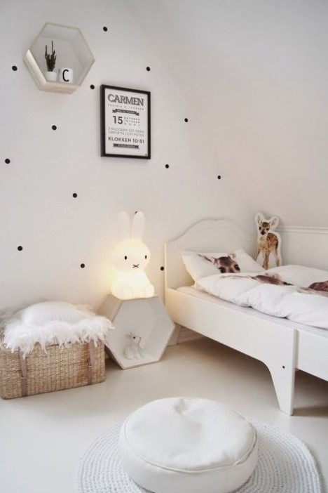 a pretty and airy Nordic kid's room with a polka dot wall, a white bed, a hex shelf, an ottoman and a rug, a baket for storage