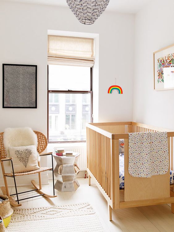 a pretty small nursery with a stained crib and a chair, some art, neutral and printed textiles and a metallic side table