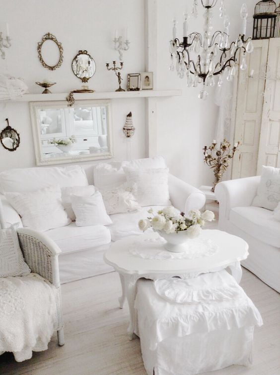a pure white shabby chic living room with stylish furniture, a crystal chandelier, mirrors and candles is wow